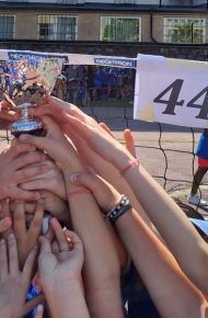 fotografia: tante mani di ragazzi sollevano una coppa:sullo sfondo una rete da pallavolo