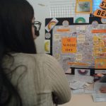 RAGAZZA DI SPALLE OSSERVA CARTELLONI ALLA FIERA DELLE IDEE