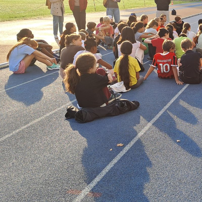alunni di spalle seduti sulla pista da corsa ascoltano le indicazioni dei docenti