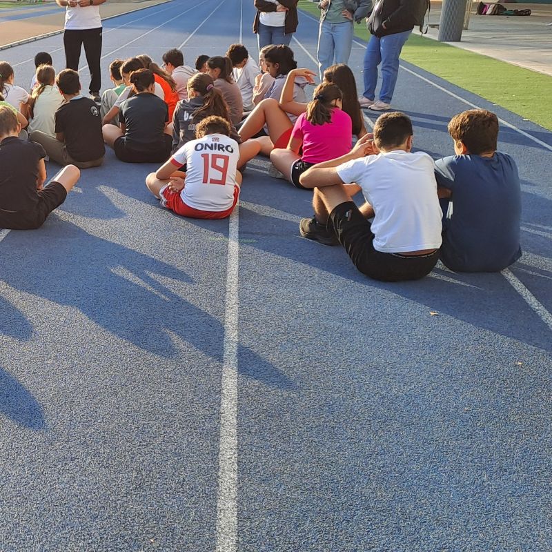 alunni di spalle seduti sulla pista da corsa ascoltano le indicazioni dei docenti
